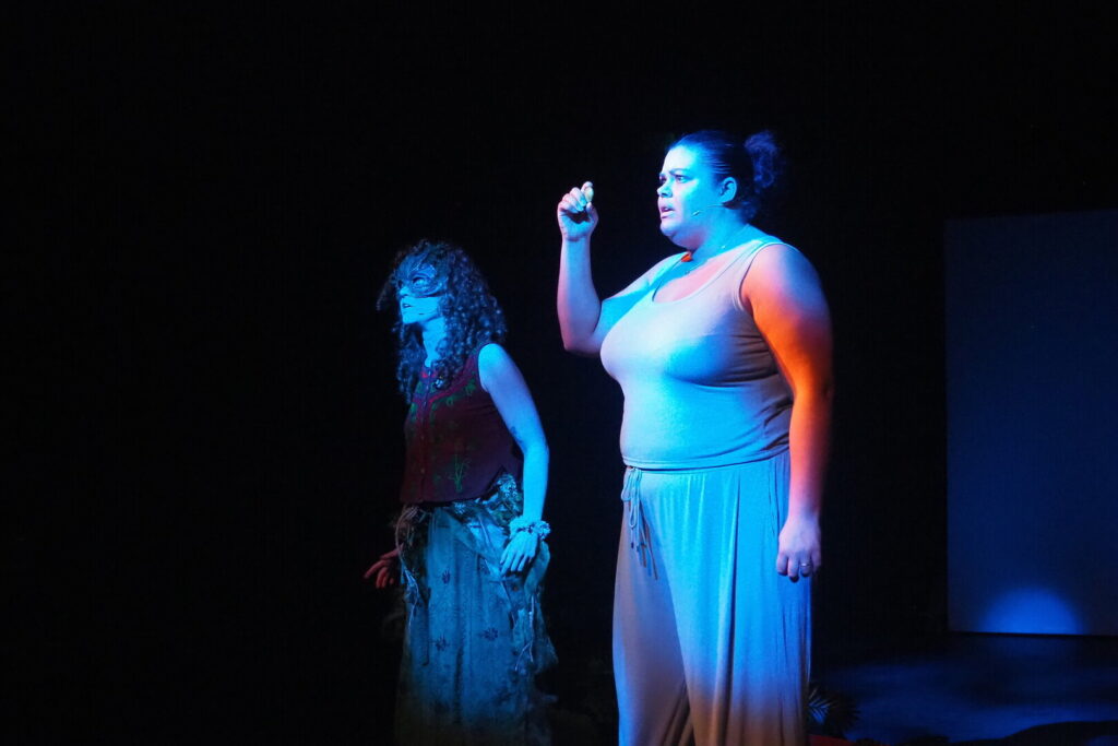 Two actors on stage during a performance of Bringing the Outside In. Both actors are in costume and lit up with stage lighting.
