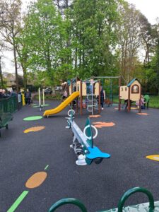 Queen Elizabeth II play area at Whartons Lane, Ashurst, with slide, climbing frames and seesaw on rubber surface under trees
