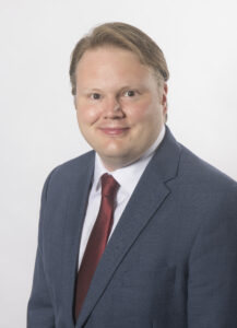 Headshot of NPA board member Dan Poole wearing a blue suit and red tie against a white background
