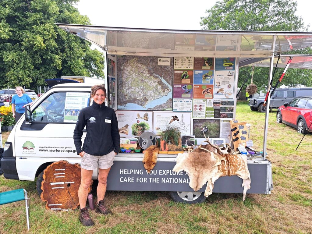 New Forest National Park staff member beside a mobile information van with wildlife posters, maps, and animal hides on display