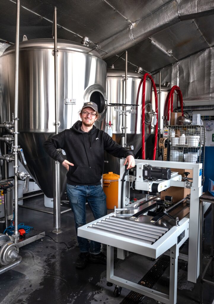 man standing in a brewery with a taping machine
