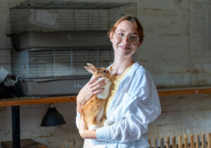 Young woman wearing a light blue shirt smiles while holding a white and ginger rabbit.