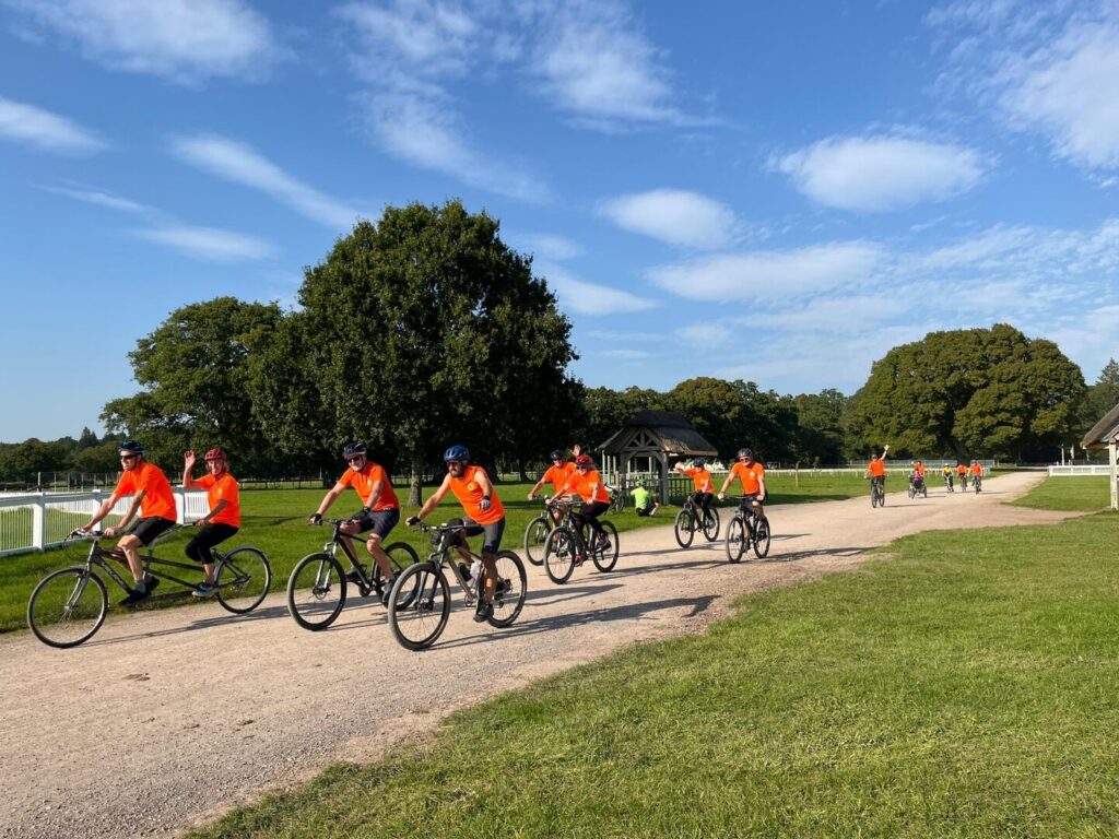 PEDALL volunteers ride in a group at Pass the PEDALL on a New Forest track with trees and a blue sky in the background.