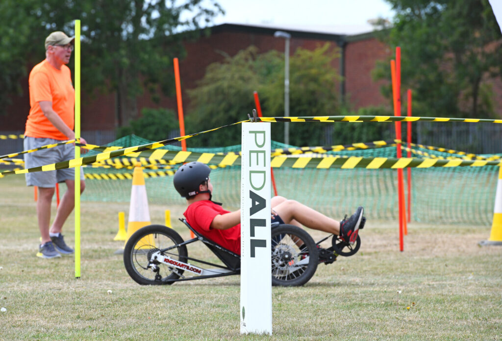 A young person rides on an adapted cycle on PEDALL - New Forest Inclusive Cycling's track at New Forest Thrive festival 2025.