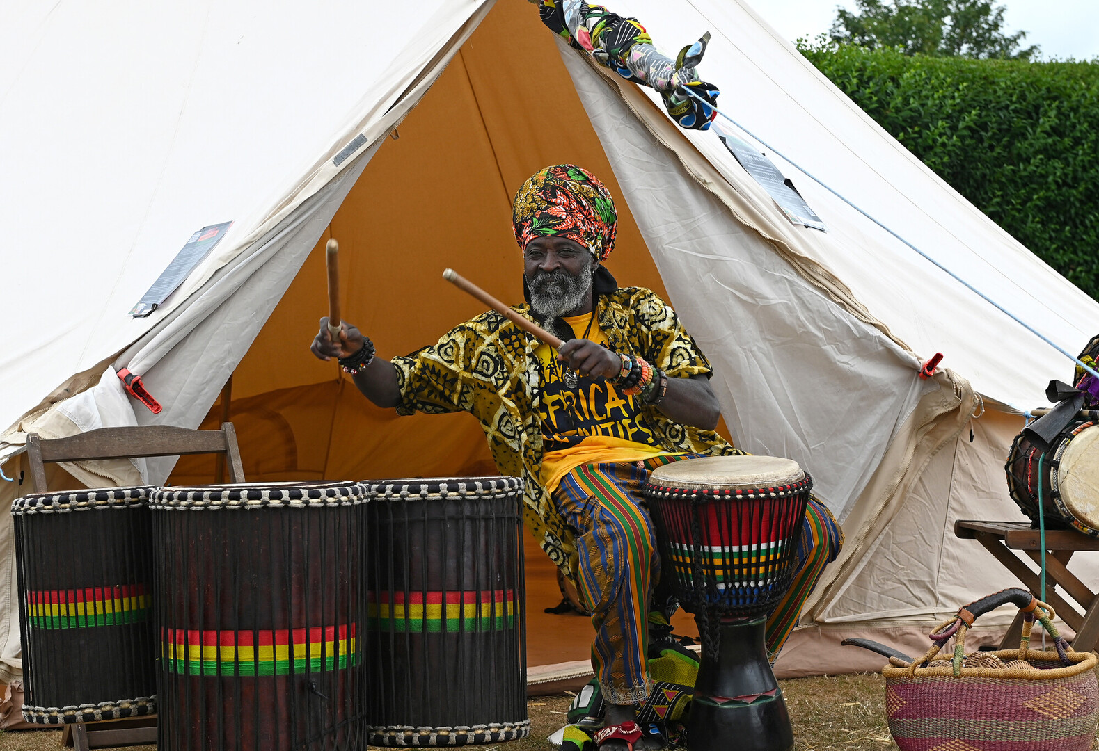 A man from African Activities is drumming in front of a tent at New Forest Thrive festival 2025.