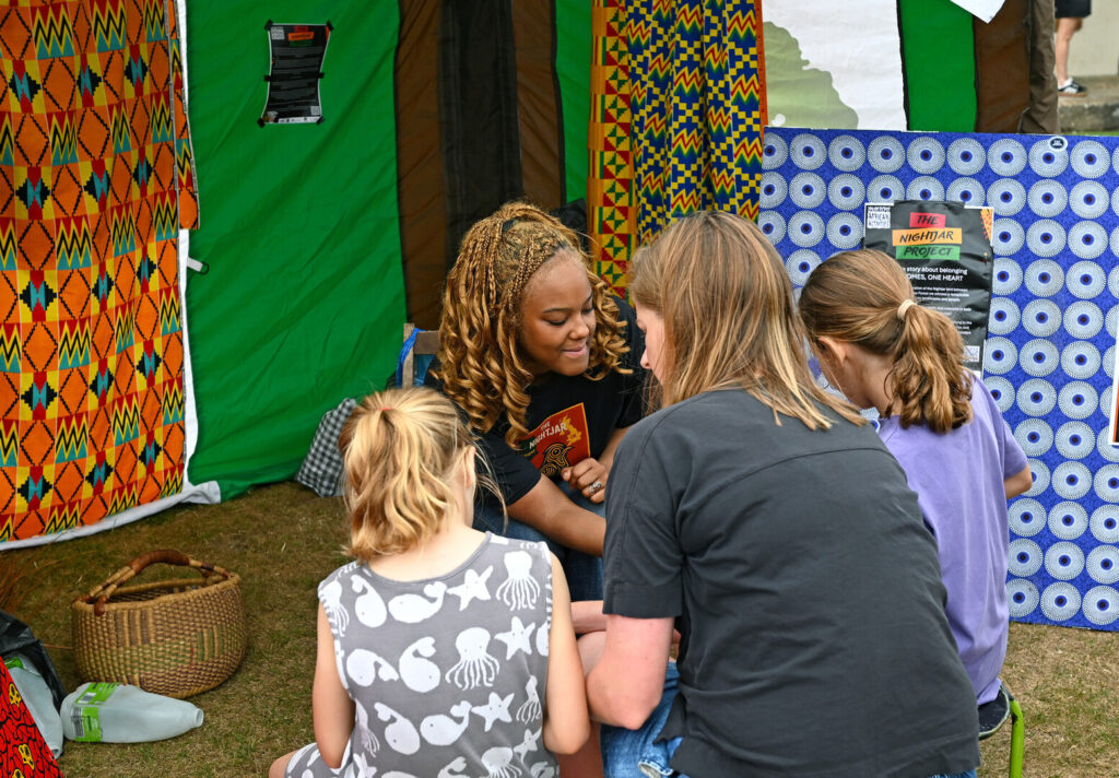 Stallholders interact with young people and a family at New Forest Thrive festival 2025.