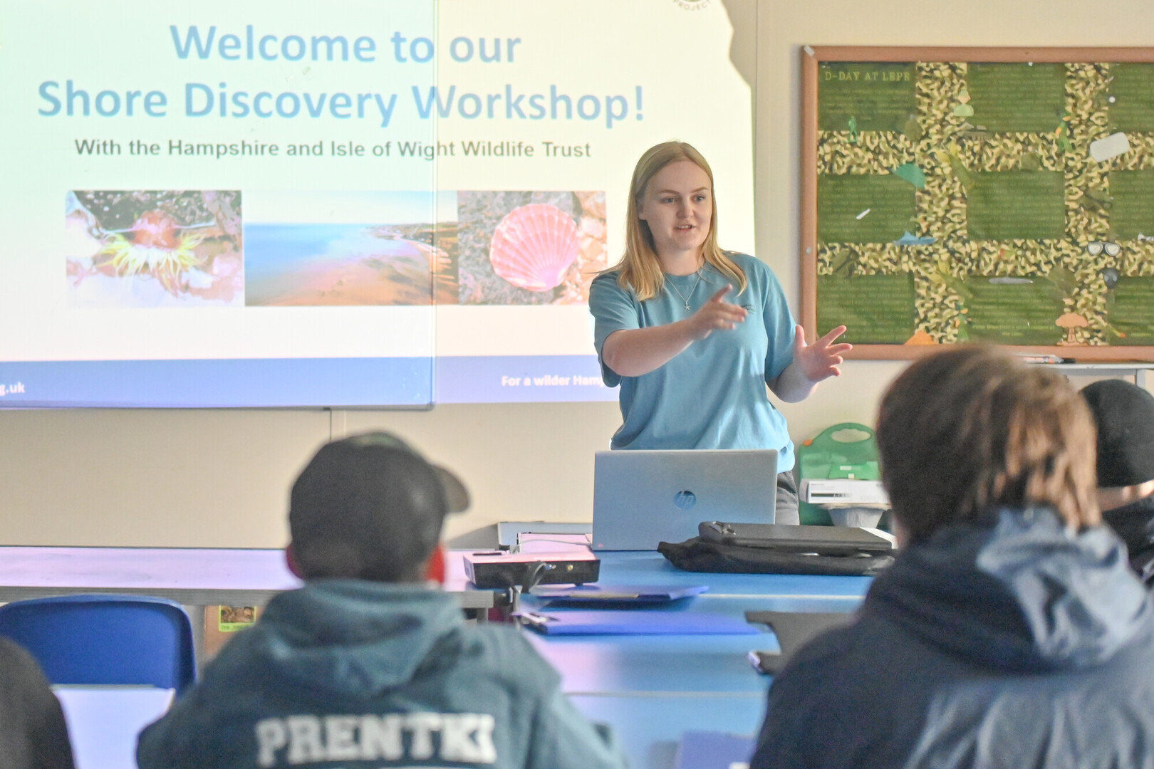 Workshop leader presents Shore Discovery Workshop to seated junior rangers, with projector slide and laptop.