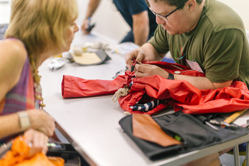 Man repairs a red jacket at a community repair cafe while a woman watches across the table