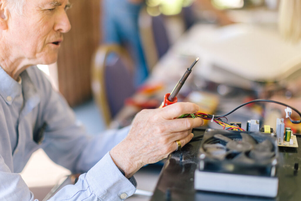 Person soldering wires on an electronic device circuit board at a repair cafe workshop
