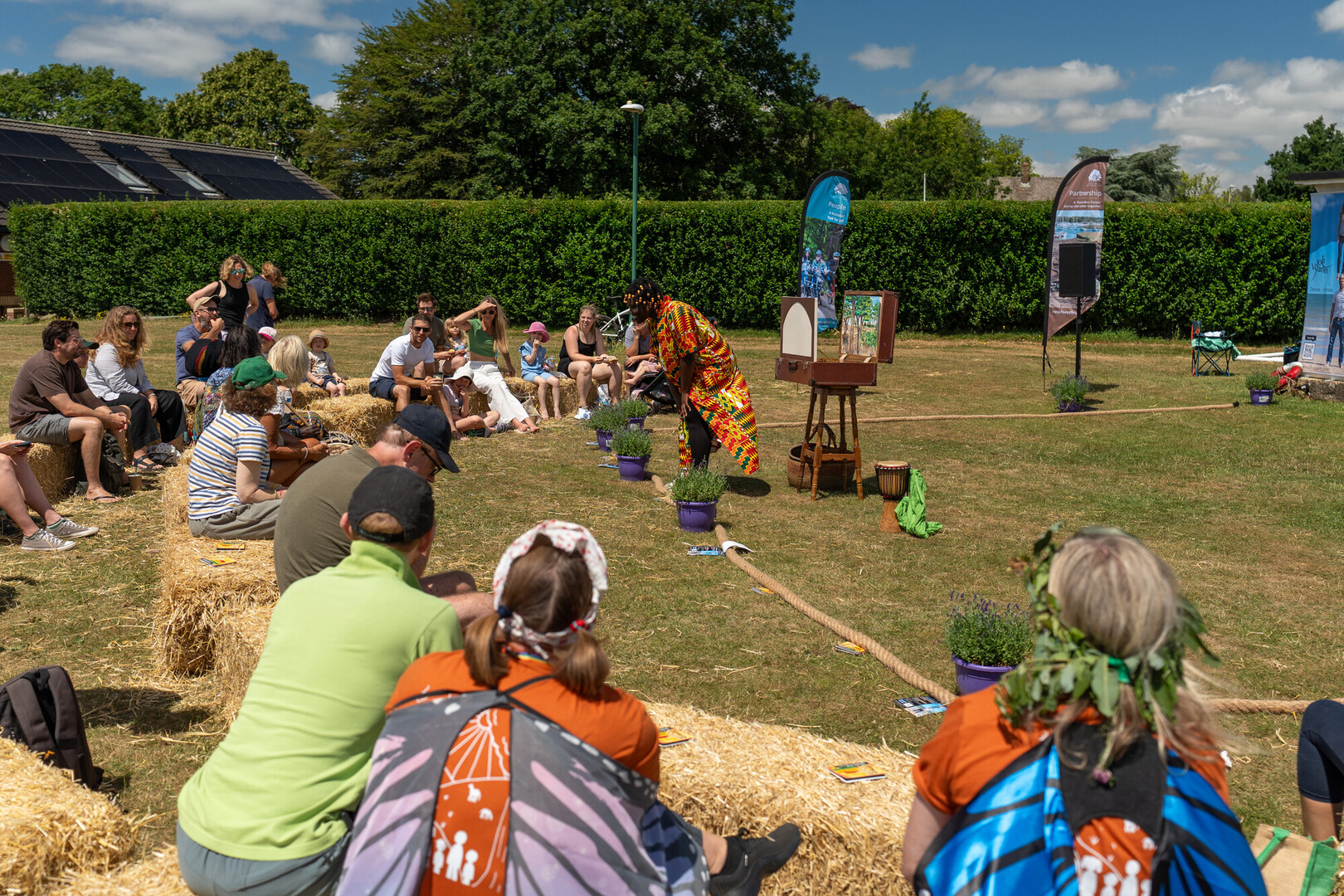 A group of people sat on hay stacks watching a performance at an outdoor community festival