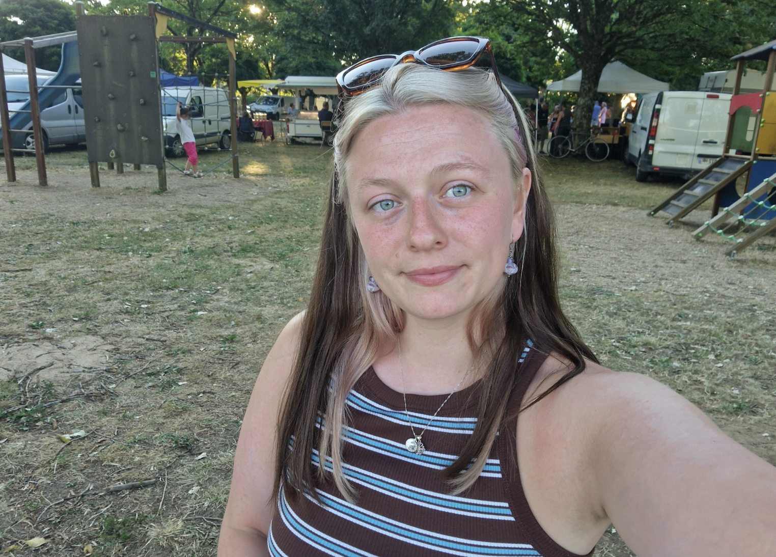 Young woman taking a selfie outside with grass behind her, wearing a stripy top