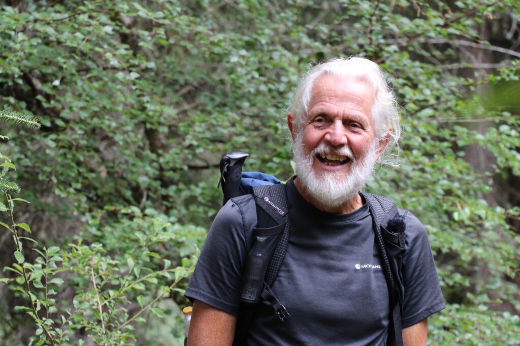 Man smiling with backpack against vegetation