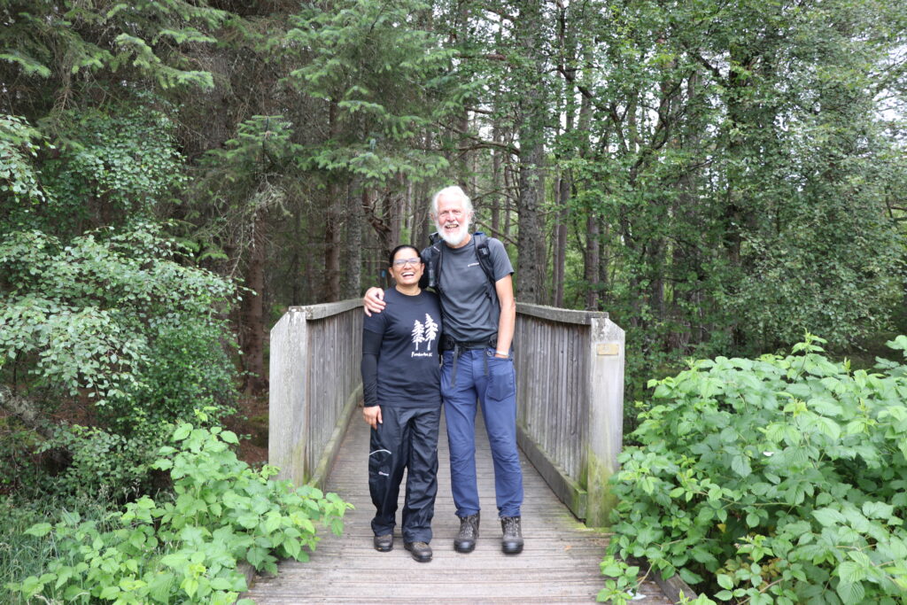Man and woman smiling standing on a bridge in a woodland