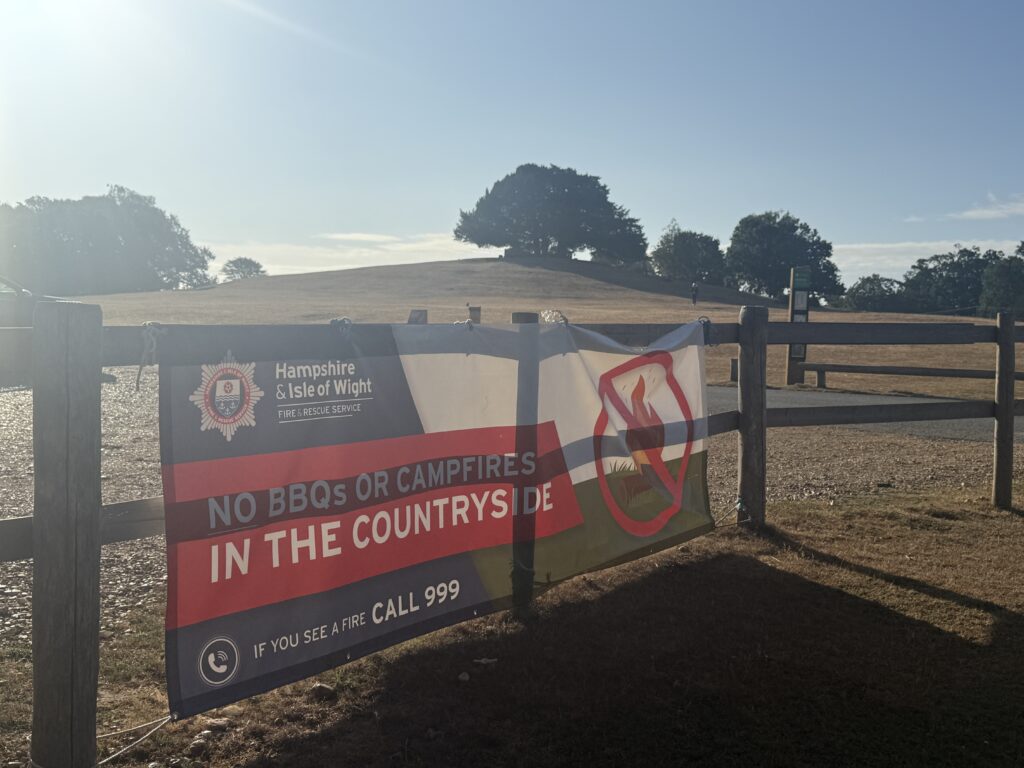 Hampshire & Isle of Wight Fire and Rescue Service banner on fence warning “No BBQs or campfires in the countryside” near dry field