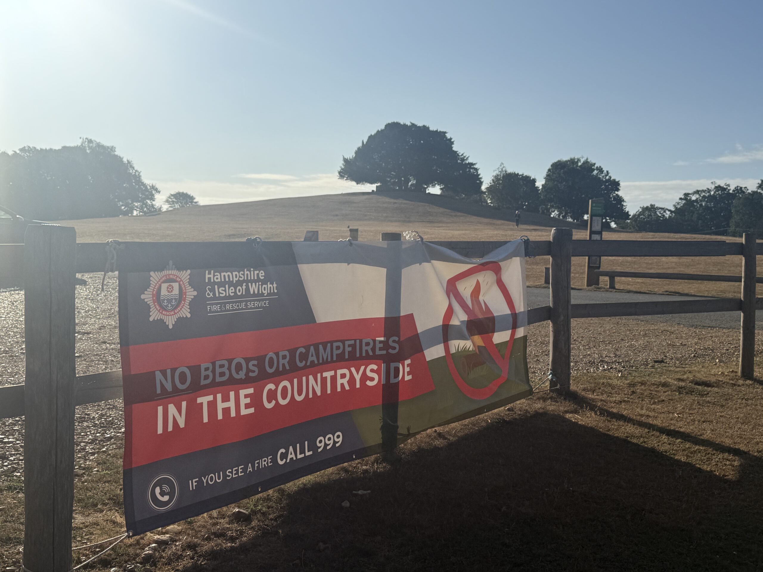 Hampshire & Isle of Wight Fire and Rescue Service banner on fence warning “No BBQs or campfires in the countryside” near dry field