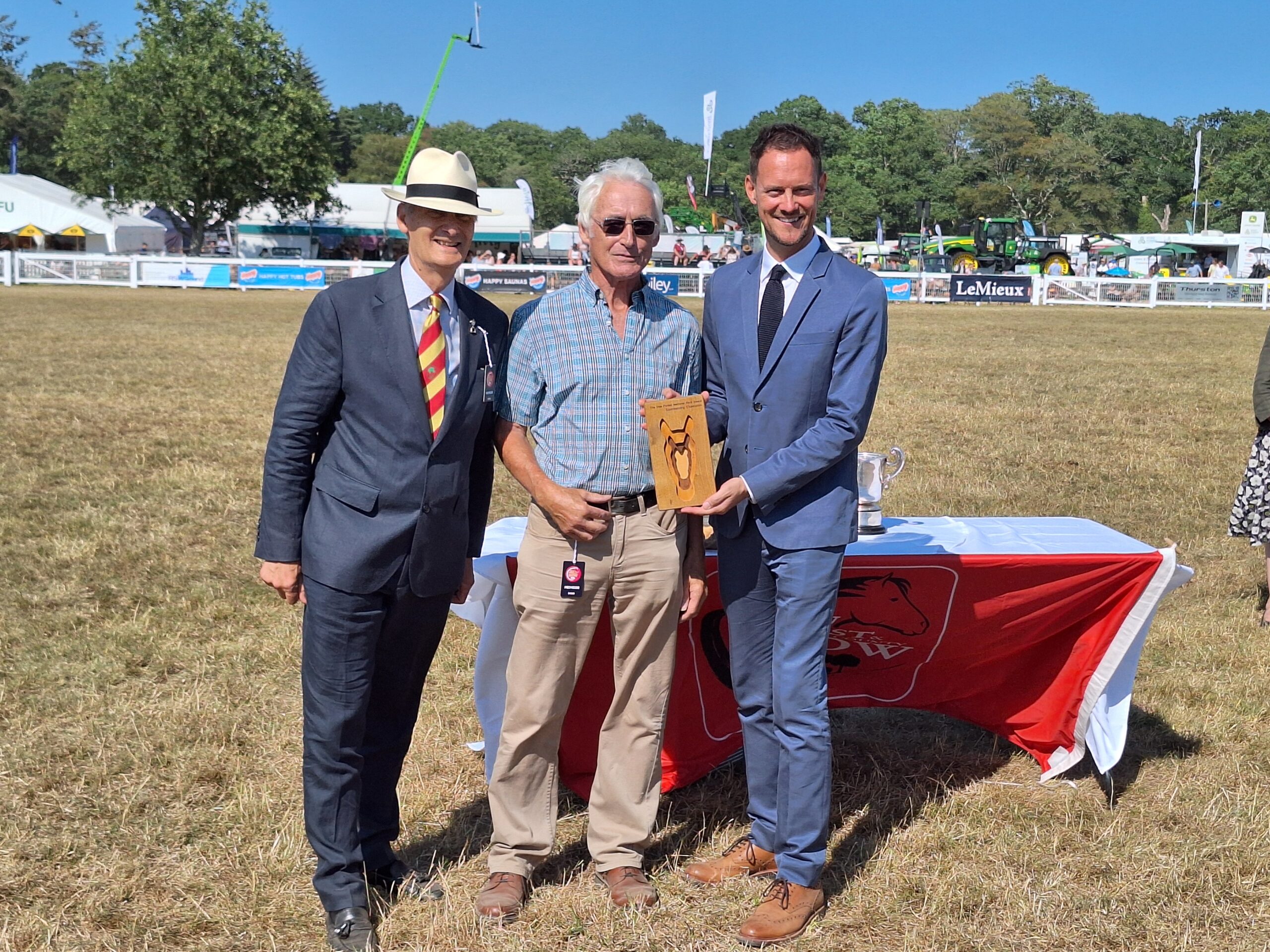 Richard Deakin accepts a wooden award plaque from a man in a blue suit at the New Forest Show 2026, standing on a showground field