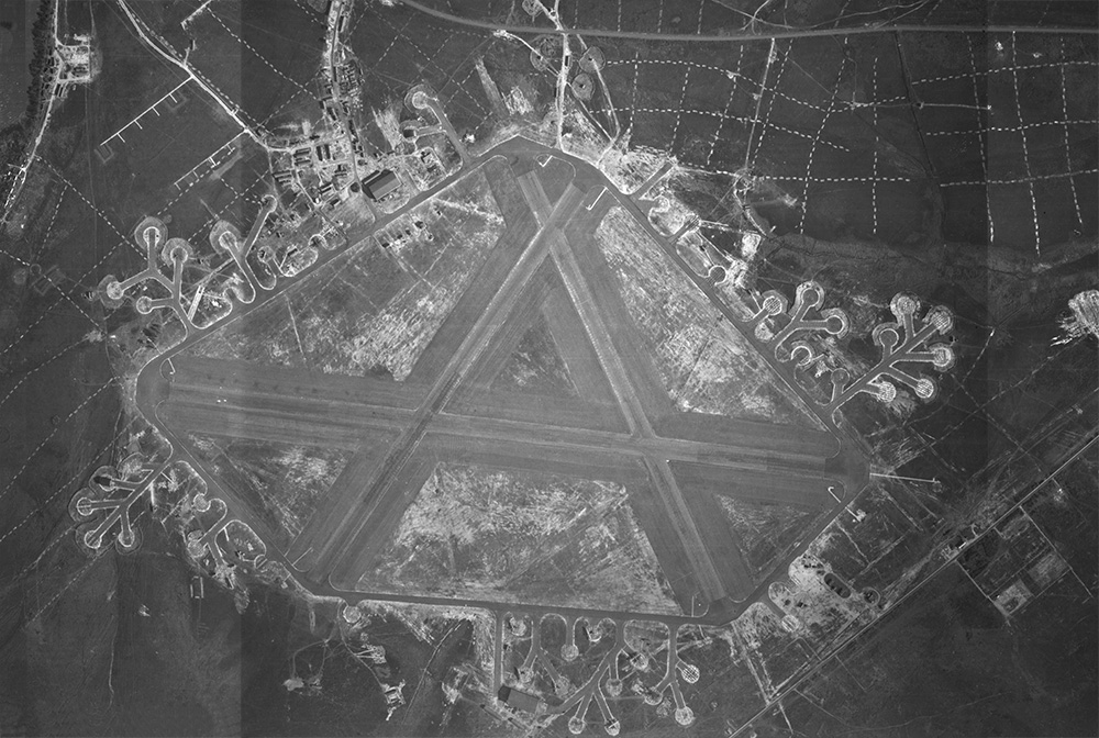 Aerial view of a WWII airfield with three intersecting runways and looping taxiways and dispersal bays around the perimeter