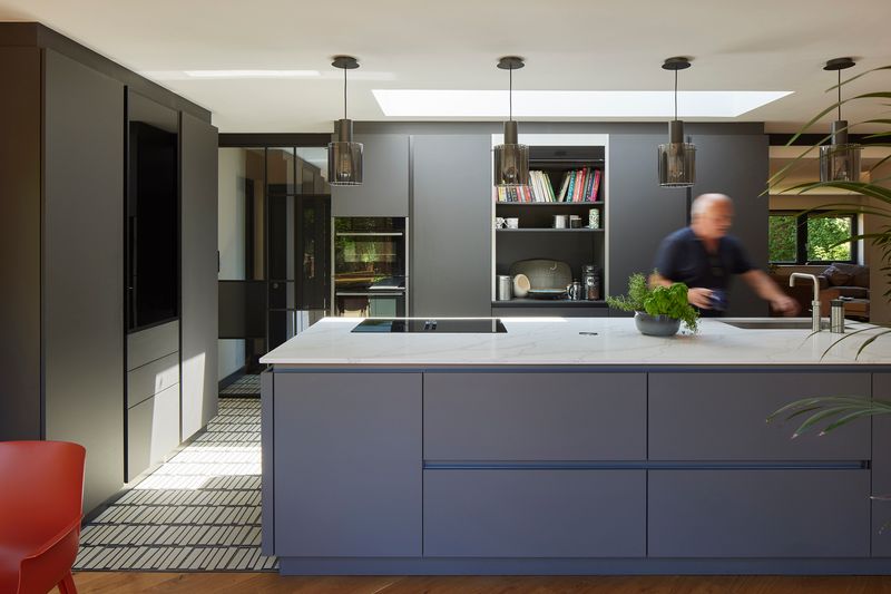 Modern kitchen with large island and black cabinetry, three pendant lights, skylight, and a blurred person moving in the background