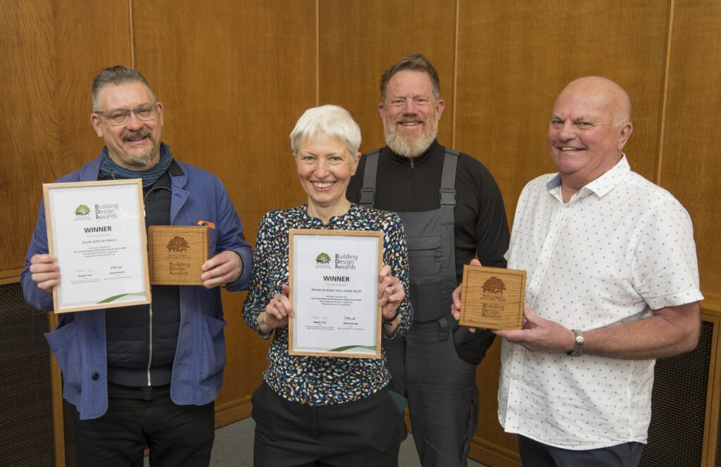 Four award winners holding New Forest National Park Authority Building Design Awards certificates and wooden plaques indoors