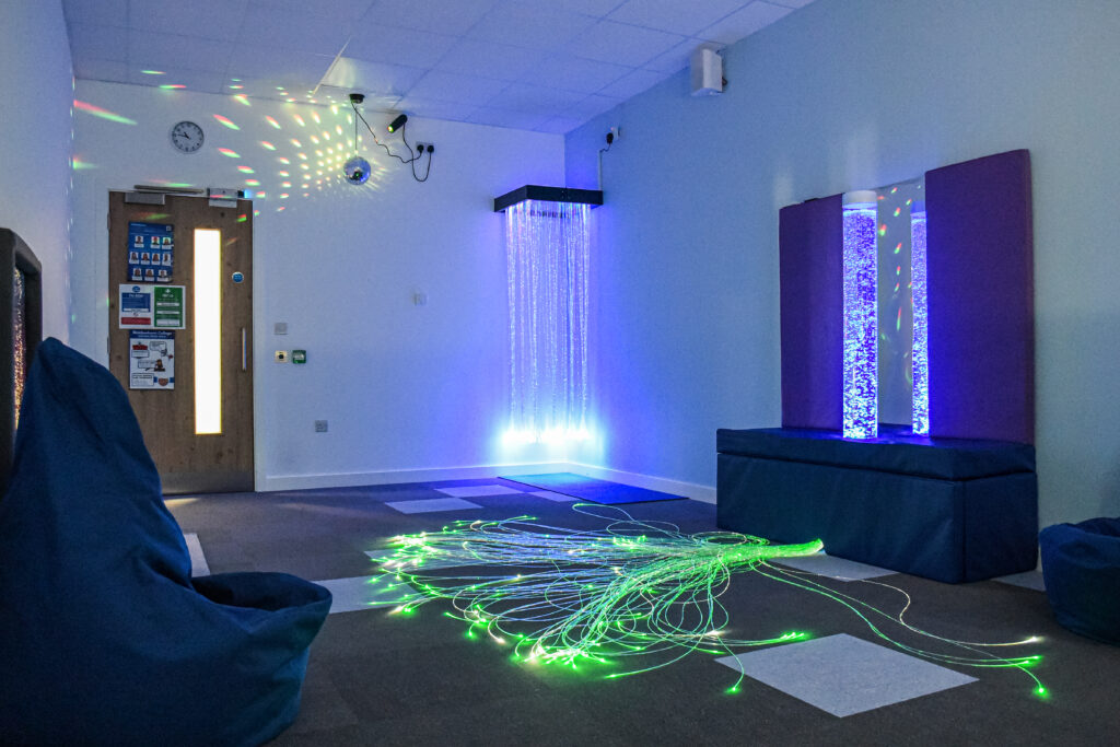 Sensory room at Brock College with blue bubble tube, fibre optic floor lights, beanbag seating, and disco ball reflections on walls
