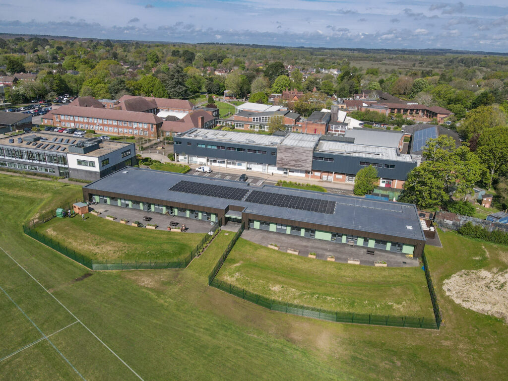 Aerial view of Brock College campus buildings with solar panels, next to a fenced sports field and surrounding trees and houses