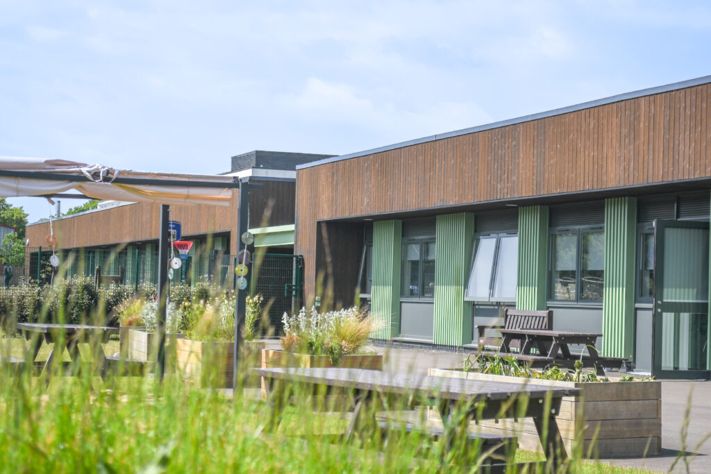 Exterior of Brock College Foundation and Independence Hub with wood cladding, green columns, large windows, and picnic benches in courtyard