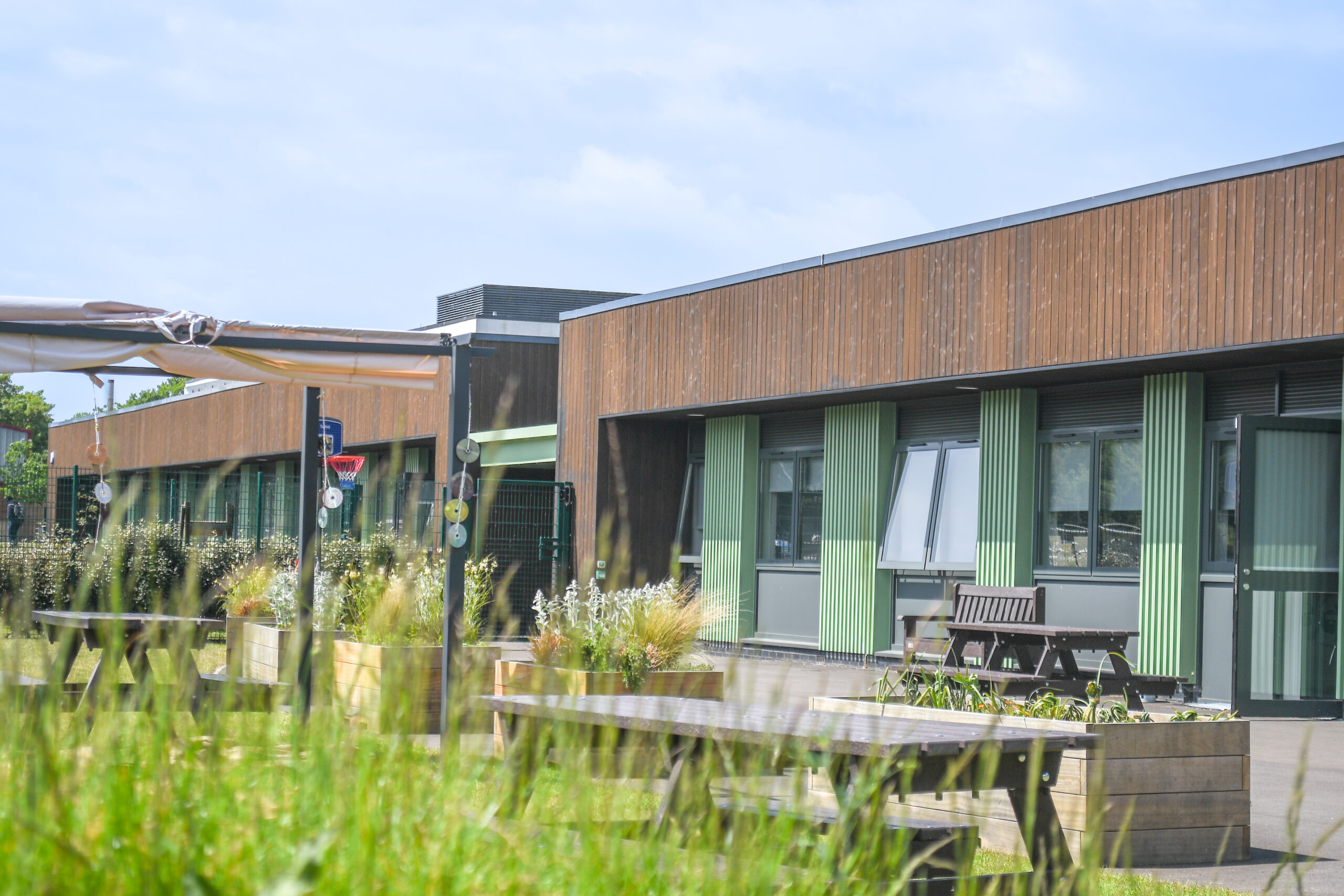 Exterior of Brock College Foundation and Independence Hub with wood cladding, green columns, large windows, and picnic benches in courtyard