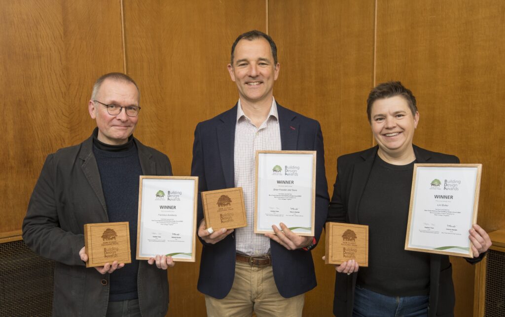 Three award winners holding New Forest National Park Building Design Awards certificates and wooden plaques in front of wood paneling
