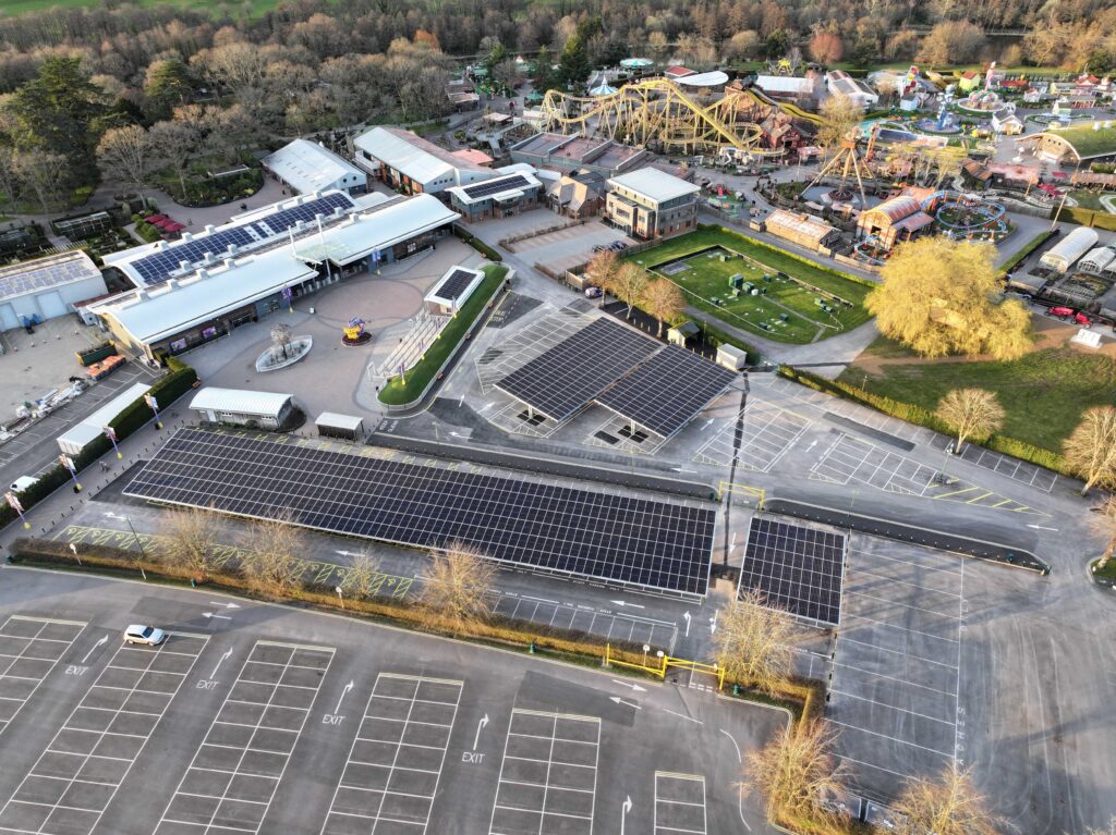 Aerial view of Paultons Park showing solar panel carport canopies over a parking lot, with theme park rides and trees behind