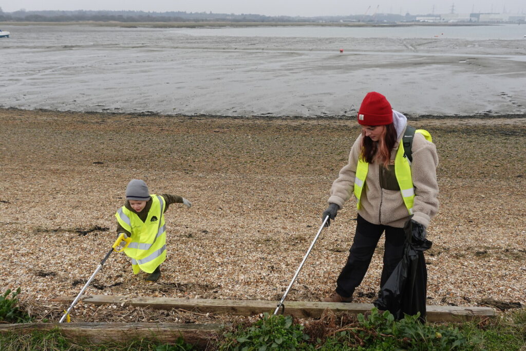 A woman and a child litter picking on a beach. They are wearing warm clothing and high vis. 