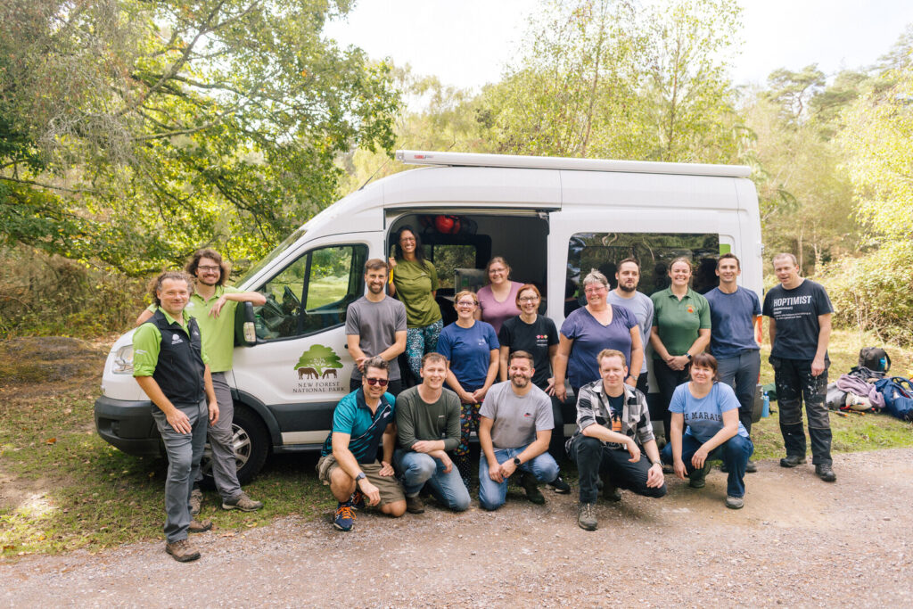 A team of corporate volunteers stand and kneel in front of the New Forest NPA's welfare van